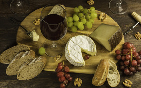 Сыр на столе с орехами, хлебом, виноградом и бокалом вина