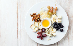 Chunks of cheese on a plate with nuts, grapes, honey and blackberries