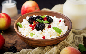 Творог с ягодами в деревянной миске на столе с яблоками