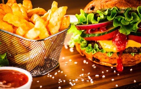 Аппетитный сочный гамбургер на доске с картошкой фри и соусом