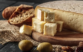 Сыр нарезан кубиками на столе с хлебом и оливками