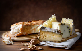 Different types of cheese on the table with loaf and walnuts