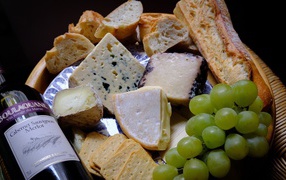 Different types of hard cheese on a plate with white grapes and wine