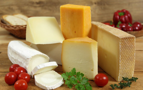 Different types of hard cheese on a table with tomatoes and parsley