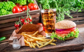 French fries, hamburger, cola and tomatoes on the table