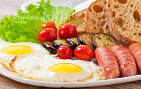 Fried eggs on a plate with sausages, vegetables and bread