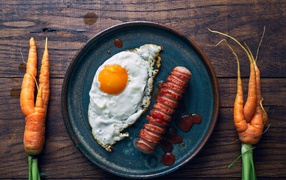 Fried eggs with sausage on the table with carrots