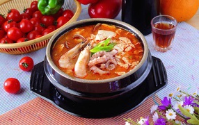 Тарелка красного супа с морепродуктами на столе с овощами 
