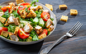 Салат с овощами, сухариками и курицей и на столе с вилкой