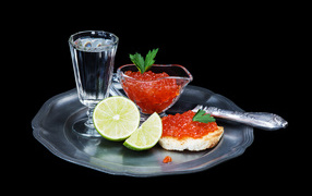 Sandwiches with red caviar on a tray with a glass of vodka and lime