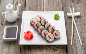 Sushi on a large white plate with wasabi sauce and ginger on a table with soy sauce