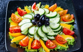 Tomato, cucumber and pepper salad on a plate with lettuce and olives