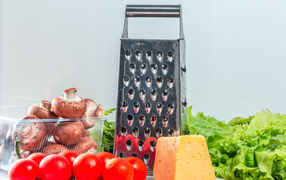 Tomatoes on a table with a grater, mushrooms, lettuce and cheese
