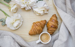 Two croissants with a cup of coffee on a table with white buttercups