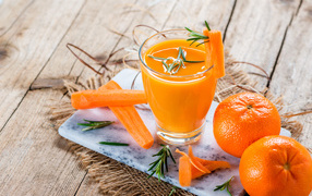 Два апельсина на столе со стаканом морковного сока