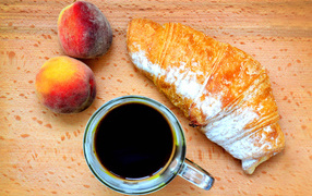 Two peaches on a table with coffee and a croissant