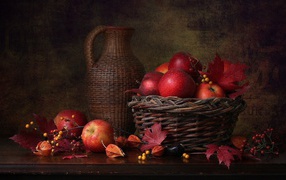 Basket with red apples on the table with a jug