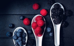 Blueberries, raspberries and blackberries on white spoons