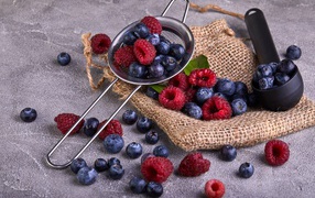 Blueberries and raspberries on a table with a strainer
