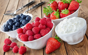 Raspberries, blueberries and strawberries on a table with cottage cheese