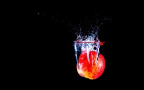 Красное яблоко падает в воду на черном фоне