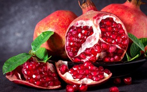 Red pomegranates with grains and green leaves on a gray background