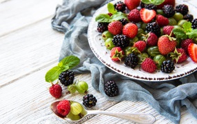 Спелые ягоды крыжовника, ежевики, малины и клубники на тарелке