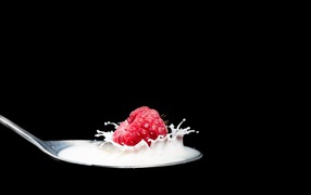 Спелая красная малина с ложке с молоком на черном фоне