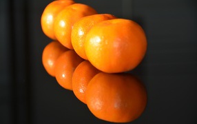 Желтые мандарины отражаются в поверхности стола 