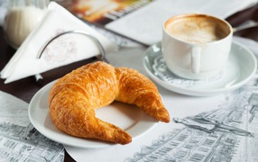 Croissant on a white plate with a cup of cappuccino