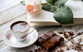 Чашка кофе на столе с шоколадом, книгой и розой