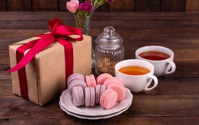 A gift with a red ribbon on the table with macaroons and tea