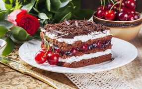 Кусок торта с вишней, шоколадной крошкой на столе с розой