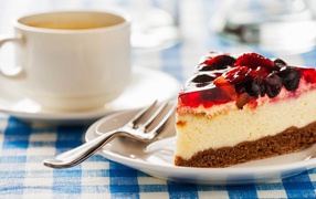 Кусок чизкейка с ягодами и желе на столе с чашкой кофе