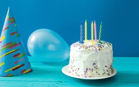Celebratory cake with candles, a ball and a cap on a blue background