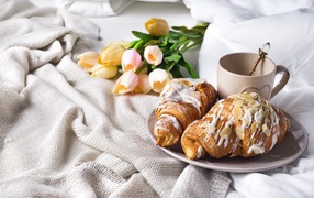 Croissants on a bed with coffee and a bouquet of tulips