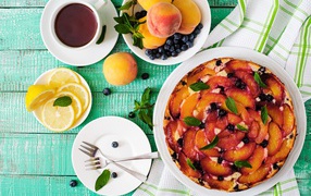 Вкусный пирог со сливами на столе с чаем, лимоном и персиками