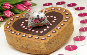 Торт в форме сердца с фигурками крыс на столе со свечами и букетом тюльпанов