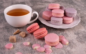 Сладкий десерт макарун на столе с чашкой чая, сахаром и лепестками розы