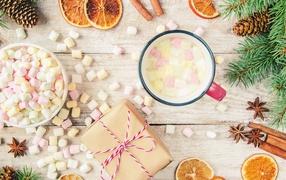 Кружка горячего напитка на столе с маршмеллоу, пряностями и подарком