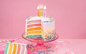 Разноцветный праздничный торт со свечами на розовом фоне