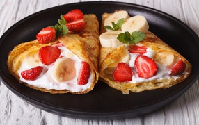 Pancakes with sour cream, bananas and strawberries in a pan