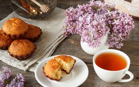 Сладкие кексы на столе с чаем и букетом сирени