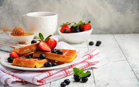 Sweet waffles with blueberries and strawberries on the table with honey and tea