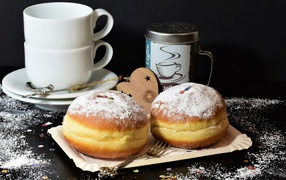 Two donuts with powdered sugar on a black background with white cups