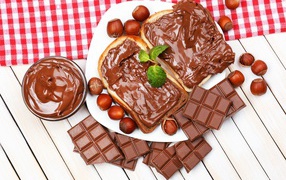 Two pieces of chocolate spread on a table with chocolate and nuts