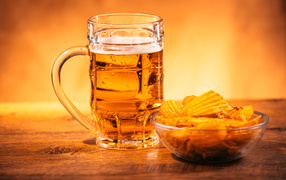 A glass of beer with a plate of chips on the table