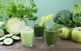 Зеленый овощной смузи в стаканах на столе со свежими овощами и яблоками