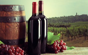 Две бутылки красного вина на столе с виноградом и бочкой