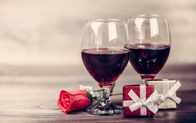 Два бокала вина на столе с подарками и красной розы 